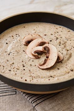 a pan filled with soup and mushrooms on top of a cloth covered tablecloth next to a wooden utensil