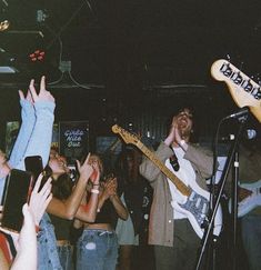 a group of people holding their hands up in the air while singing and playing guitar