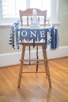 a wooden chair with a blue and white one banner on it's back sitting in front of a window