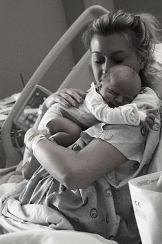 a black and white photo of a woman holding a baby in her arms while sitting in a hospital bed