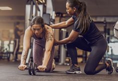 two women doing push ups with dumbbells in a gym together, one is squatting and the other is standing