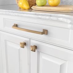 a kitchen with white cabinets and marble counter tops, gold pulls on the handles that match the cabinet door knobs