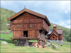 an old log cabin sits in the middle of a grassy field next to two wooden buildings