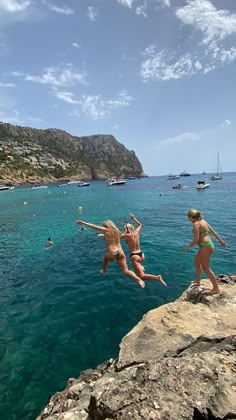 two girls jumping off rocks into the ocean