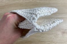 a hand holding a crocheted white object on top of a wooden table next to a piece of wood