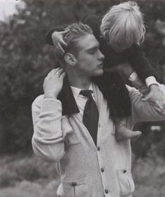 a man holding a small child in his arms while wearing a suit and tie with trees in the background