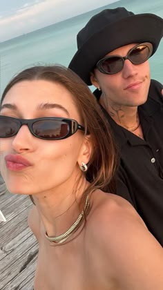 a man and woman taking a selfie on a pier next to the ocean in sunglasses