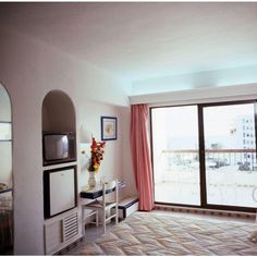 a hotel room with a bed, television and balcony overlooking the ocean in front of it