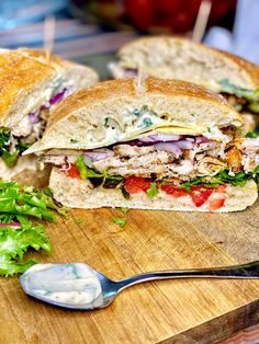 a cut in half sandwich sitting on top of a wooden cutting board next to a spoon