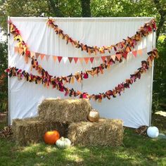 hay bales and pumpkins are arranged in front of a white backdrop with bunting