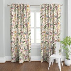 a white chair sitting next to a window covered in pink and green floral curtain panels