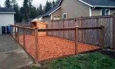 a fenced in area with wood chips on the ground next to a house and yard