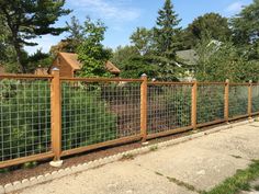 a wood and wire fence is next to a sidewalk in front of a house with trees on the other side