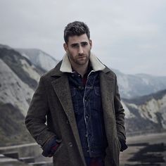 a man standing in front of mountains with his hands on his hips and looking at the camera