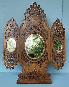 an ornate wooden clock with three mirrors on it's face and the reflection of trees in