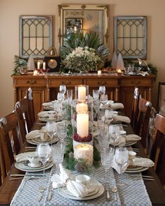 a dining room table set for christmas dinner with candles and greenery on the side