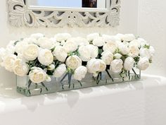 white flowers are arranged in glass vases on a shelf next to a mirror and wall