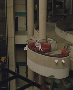 a man sitting in a red chair on top of a circular bench next to a tall building