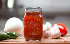 a jar filled with red sauce sitting on top of a wooden cutting board next to vegetables