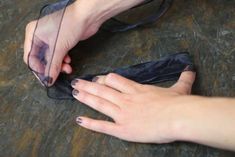 a woman's hands holding something on top of a piece of black material with sheer fabric