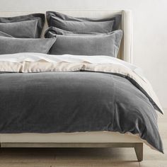 a bed with grey and white linens in a minimalistic style bedroom, including the headboard and foot board