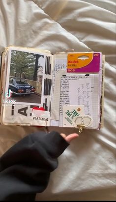 an open book with pictures and writing on it, sitting on a bed next to a person's hand