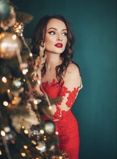 a woman in a red dress standing next to a christmas tree