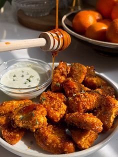 a white plate topped with fried food next to a bowl of ranch dressing and oranges