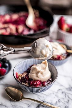 two bowls filled with fruit and ice cream on top of a marble counter next to spoons