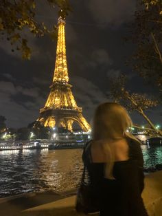 a woman standing in front of the eiffel tower at night with her back turned to the camera