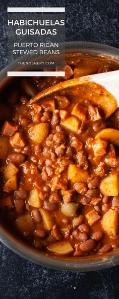 a bowl filled with beans and potatoes on top of a table next to a spoon