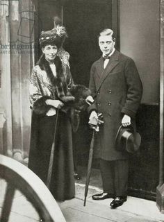 an old black and white photo of two people standing in front of a building, one holding