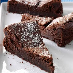 chocolate brownies with powdered sugar on top sit on a white plate, ready to be eaten