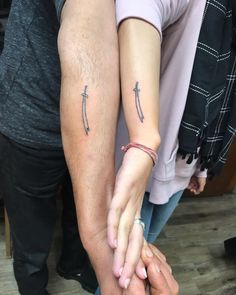 two people holding each other's hands with small tattoos on their arms and fingers