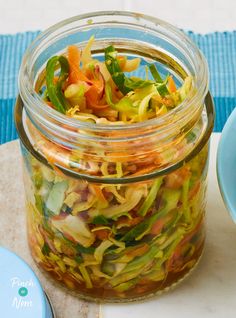 a glass jar filled with vegetables sitting on top of a table next to a blue plate