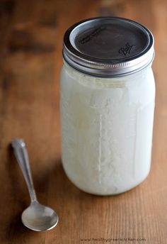 a spoon sitting next to a glass jar filled with white liquid on top of a wooden table