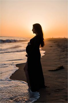 a pregnant woman standing on the beach at sunset