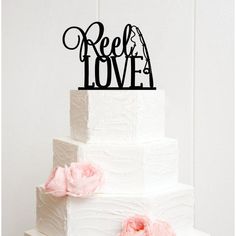 a three tiered cake with pink flowers on the side and an acrylic sign that reads reela love