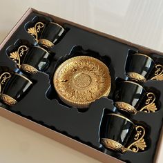 a set of black cups and saucers in a box with gold trimmings