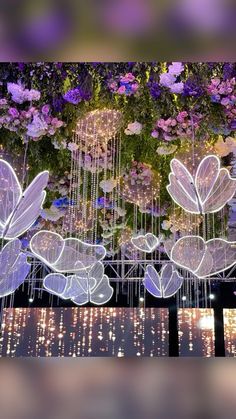 some lights that are hanging from the ceiling in front of flowers and plants on display