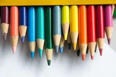 several colored pencils lined up on top of a white piece of paper next to a yellow pencil holder