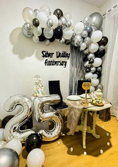 a table with silver and black balloons in the shape of numbers on it, next to a balloon arch that says 25th wedding anniversary