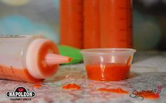 an orange liquid in a small container next to a plastic cup with the lid open