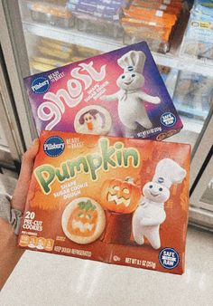 a person holding up two boxes of pumpkin snacks in front of a refrigerator door with frosting on it