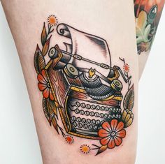 an old fashioned typewriter tattoo on the leg, with flowers around it and leaves