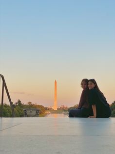 two women are sitting on the ground in front of the washington monument at sunset or sunrise