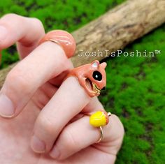 a person holding a tiny animal ring in their hand with grass behind it and a tree branch on the other side