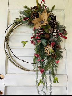 a wreath is hanging on the door with pine cones, berries and other greenery