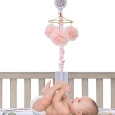 a baby laying on its back in a crib next to a pink and white mobile