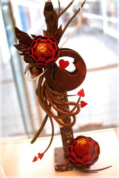 a sculpture made out of metal and paper with red flowers on the top, in front of a window